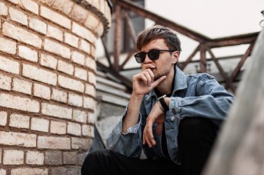 Siyah güneş gözlüklü, modaya uygun mavi kot ceketli yakışıklı hippi şehirde tuğla duvarın yanındaki eski bir merdivende oturmaktan zevk alıyor. Havalı adam bir bahar günü açık havada dinleniyor..