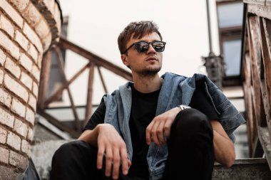 Siyah pantolonlu, şık siyah gözlüklü modern hippi adam şehrin tuğla duvarının yanındaki eski bir merdivende rahatlıyor. Havalı adam hafta sonlarını dışarıda geçirmeyi seviyor..