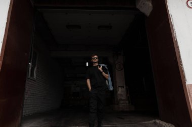 Siyah pantolonlu, modaya uygun, siyah gözlüklü, modern stil sahibi hippi adam karanlık binadan çıkıyor. Amerikan modasına uygun bir adam şehirde dolaşıyor. Sokak tarzı.