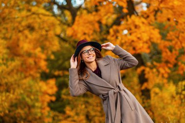 Güzel bir gülüşü olan, şık bir şapkası olan, şık gözlüklü, şık bir şapkası olan, güzel, genç bir kadın sonbahar parkında hafta sonunun keyfini çıkarıyor. Oldukça mutlu hippi kız dışarıda rahatlıyor..