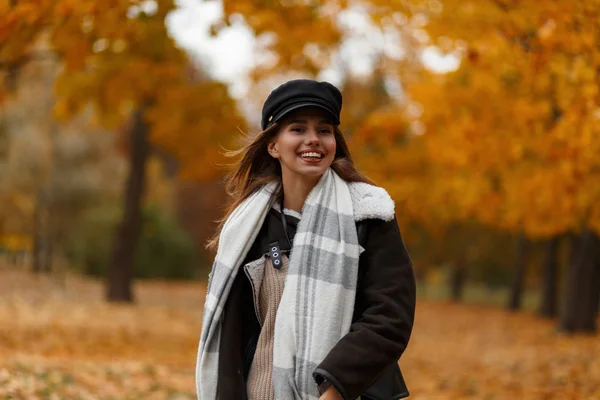 Jovem mulher alegre em outerwear elegante em um chapéu elegante com um cachecol vintage caminha no parque e desfruta da paisagem de outono. Menina feliz com um sorriso bonito viaja na floresta com folhagem amarela . — Fotografia de Stock