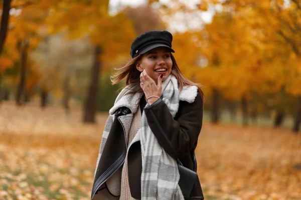 Cute szczęśliwa młoda kobieta w stylowej czarnej czapce w brązowym vintage kurtka z ciepłym modnym szalikiem z pięknym uśmiechem spacery w jesiennym parku. Atrakcyjna wesoła dziewczyna w lesie. Styl sezonu. — Zdjęcie stockowe