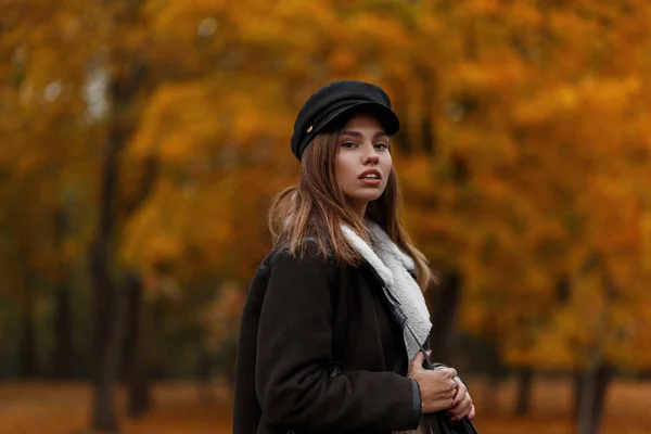 Porträt einer europäischen jungen Frau mit trendigem Hut und Visier in einer warmen braunen Jacke auf orangefarbenem Laub im Wald. Nettes Mädchen. neue Kollektion lässiger Oberbekleidung für Frauen. — Stockfoto
