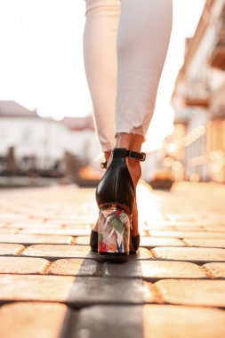 Beyaz kotlu, zarif deri sandaletli kadın bacakları gün batımında şehirde yürüyor. Üst görünüm