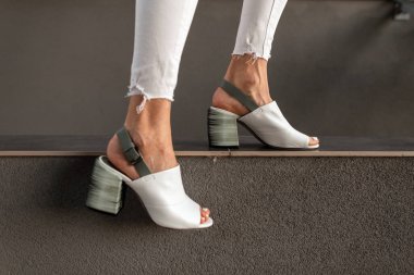 Açık havada klasik gri duvarın yanında zarif beyaz deri sandaletleri olan kadın bacakları. Yakın plan..