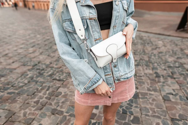 Şık kot ceketli, pembe etekli, şık çantalı bir kadın.