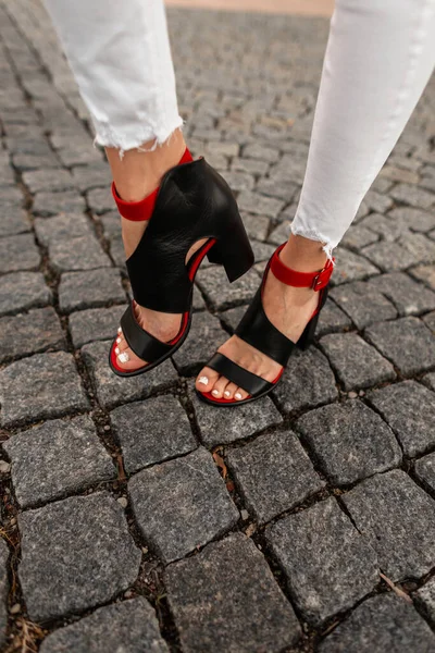 ストリートの石のタイルにスタイリッシュな赤黒の夏の靴で流行の白いジーンズの女性のファッショナブルな足のトップビュー — ストック写真