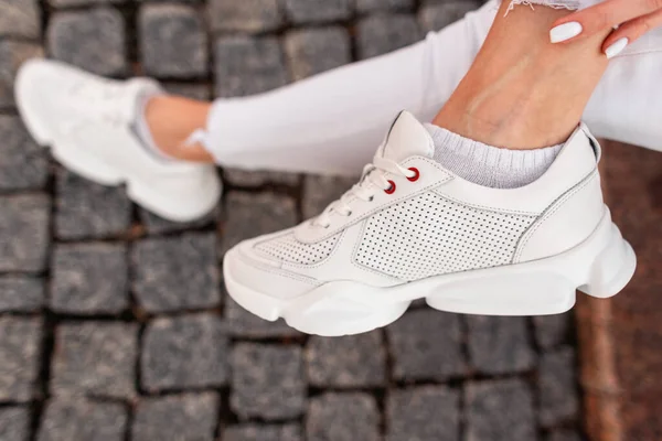 Kadın bacağında şık beyaz spor ayakkabıları, yakın plan..