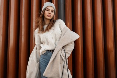 Modern bir duvarın yanında poz veren şık bir genç bayan model. Şık giyinmiş çekici bir kız şehirde duruyor. Yeni bahar koleksiyonu. Biçim.