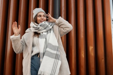 Şehirdeki metal bir duvarın yanında poz veren, kalın, modaya uygun örgü elbiseli, güzel, komik genç bir kadın. Çekici, mutlu, güzel bir gülüşü olan manken bir bahar günü açık havada dinlenmeyi sever..