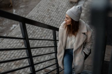 Şık genç elbiseli şık bir kadın metal merdivenlerden açık havada tırmanıyor. Yürüyüşe çıkmış modern kız modeli. Kadın kıyafetlerinin moda bahar koleksiyonu. Sıradan görünüş.