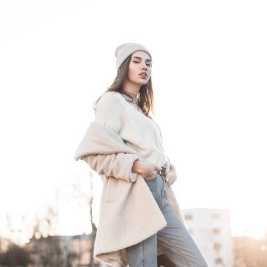 Sokakta şık, sıcak mevsimlik poz veren şık ve çekici bir kadın model. Şık genç elbiseli şirin kız, parlak beyaz kış gökyüzüne karşı şehirde yürümekten zevk alıyor..