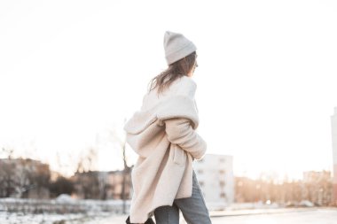 Şık örgü gri şapkalı, eski moda kürk mantolu şık bir genç bayan açık havada güneşli bir kış gününün tadını çıkarıyor. Sokaktaki son moda genç kız. Arkadan bak..