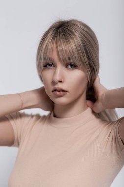 Yakın çekim stüdyo portresi. Seksi dudaklı, sağlıklı ciltli bir kadın yüzü. Oldukça çekici genç sarışın kadın saçları düzleştiriyor. Stüdyoda modaya uygun giyinen modern tatlı kız mankeni..