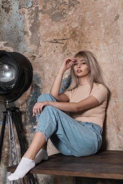 Avrupalı güzel genç bir kadın eski bir stüdyoda tuğla bir duvarın yanında dinleniyor. Moda mankeni, gündelik kıyafetleriyle siyah metal bir lambanın yanında rahatlıyor. Modayı takip eden bayan. Bahar.