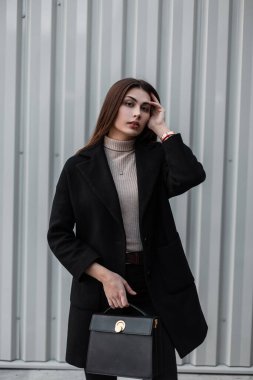 Şık kentsel model, uzun saçlı, lüks moda siyah ceketli, sokakta gümüş duvarın yanında duran deri çantalı genç bir kadın. Güzel kız modeli. Sevimli modacı bayan..