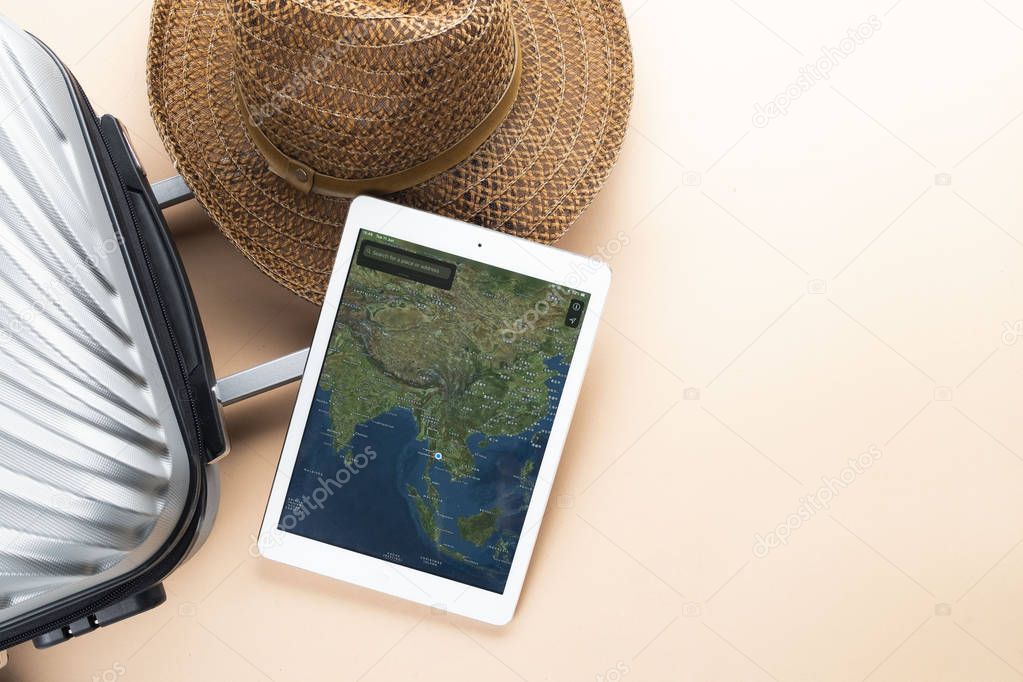 Flat lay grey suitcase with brown hat and map on gadget on paste