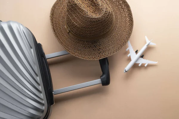 Flat lay grey suitcase with brown hat and mini airplane on paste