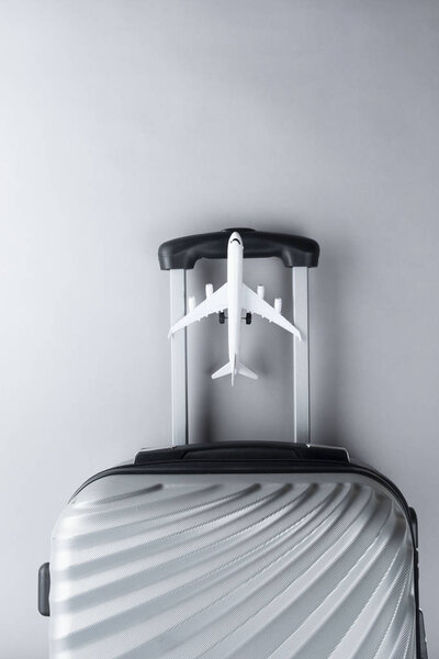 Flat lay grey suitcase with mini airplane on grey background. tr