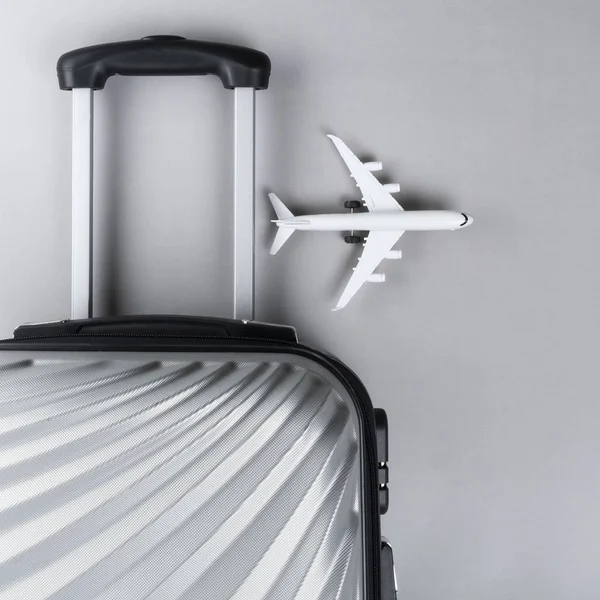 stock image Flat lay grey suitcase with mini airplane on grey background. tr