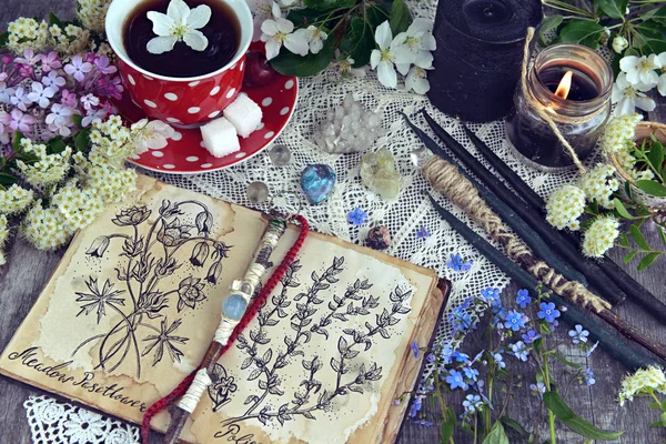 Witch book with magic and healing herbs, black candles and cup of tea. Occult, esoteric and divination still life. Halloween background with vintage objects and magic ritual