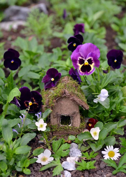 Cute fairy house with garden viola flowers. Lovely miniature house for greeting cards, wedding or birthday concept, real estate, downsizing, home ownership. Vintage summer background