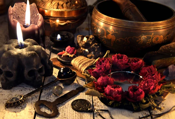 Black candles with skulls, rose mirror, metal key and singing bowl on witch table. Magic ritual. Wicca, esoteric and occult background with vintage witch objects