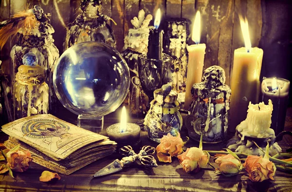 Magic crystal ball, witch bottles and burning candles on the wooden table.