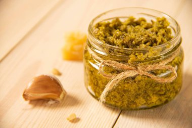 Taze İtalyan soslu fesleğen sosu cam kavanozda ahşap arka planda halat standı var. Parmesan peyniri, çam fıstığı ve sarımsak. Yakın plan.