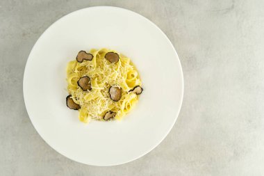 Geniş kenarlı beyaz bir tabakta yer mantarı soslu leziz İtalyan makarnası. Gri beton arka planda mantarlı fettuccine. Üst görünüm.