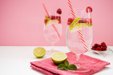 Yaz ferahlatıcı vitamin içecekleri. Limonata ve şeffaf gözlüklü ahududu pembe arka planda beyaz bir masada duruyor. Yanında bir kase ahududu, limon dilimleri ve nane yaprakları var..