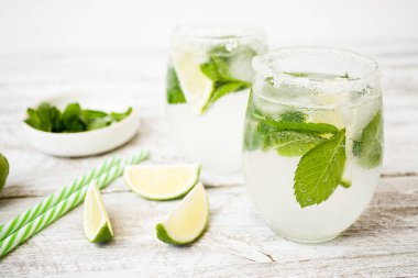 Buzlu, limonlu ve nane şekerli iki bardak. Bardakların kenarları şekerle kaplıdır. Yakınlarda taze nane yaprakları ve kireç kamaları var..