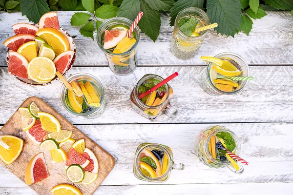 Summer champagne-based cocktails with fruits (orange, lemon, lime, grapefruit) and mint in glass mugs and glasses stand on a wooden table outdoors in the garden. Near a bowl of chopped fruit. Top view