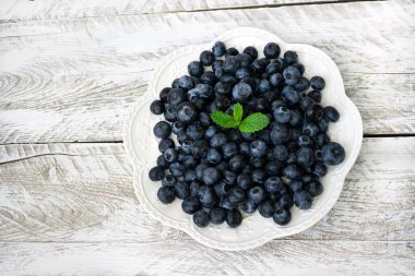 Beyaz bir tabakta olgun yaban mersini kabartmalı desenler hafif bir eski ahşap arka planda duruyor. Tabak taze nane yapraklarıyla süslenmiş. Çiğ gıda konsepti. Sağlıklı bir tatlı, atıştırmalıklar. Üst görünüm