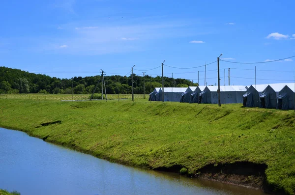 large military tents lined up along the river bank in summer on a sunny day field camp