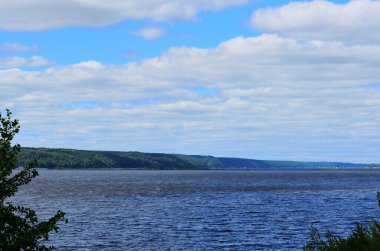 Diğer nehir kıyısının manzarası ağaçların yapraklarından çerçevelenmiş yaz bulutlu gün yatay oryantasyonu