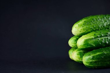 Taze yeşil salatalıklar, fotokopi alanı olan sağlıklı bir beslenme için sebzelerin siyah arka planında üst üste yatarlar.