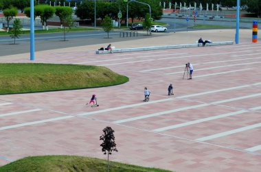 Çocukların yürüdüğü büyük şehrin bulvarı, scooterlara binmek, yetişkin erkekler bankta dinlenmek, bir adam bulvarın manzarasını kameraya çekiyor.