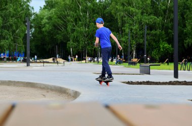 Park kaykayında mavi tişörtlü bir çocuk, ekstrem sporlar, ekstrem park, kaykay yapmayı öğrenmek, ailesiyle dinlenmek, parkta yürümek, okul çocuklarıyla yaz tatilleri, çocuk sporları.,