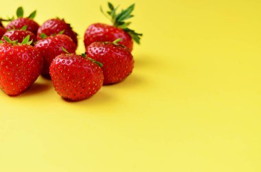 Olgun taze kırmızı çilekler sol tarafta bir sürü duruyor. Sarı arka planda bir fotokopi alanı var.