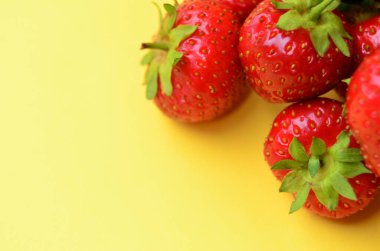 Olgun kırmızı çilek yığını sağ üst köşede duruyor. Yukarıdan sarı bir arka plan manzarası ve fotokopi alanı var.