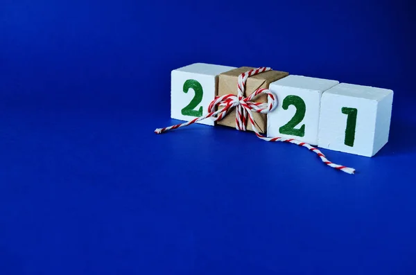 white cubes with green inscription 2021 on a blue background with a gift in craft paper with a bow with a copy space, new year, to give joys, to congratulate on the new year, holiday, Christmas,
