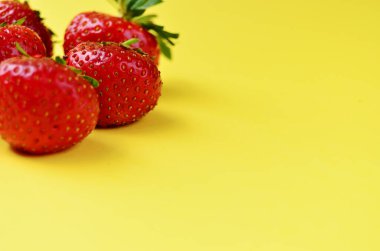 Sol üst köşede beş tane taze kırmızı çilek duruyor. Fotokopi alanı olan sarı bir zemin üzerinde. Taze ürünler, sağlıklı yiyecekler, tarım.
