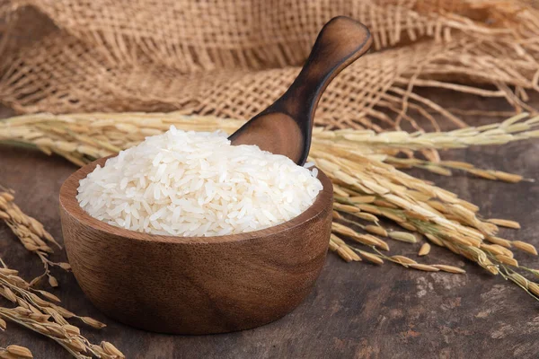 Tahta arka plandaki ahşap kasede (Thai Jasmine Rice) pirinç. Kâsede Jasmine Rice ve tahta masada çuval.
