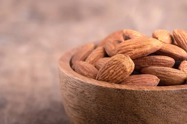 Almonds in a wooden bowl placed on a wooden table. almond nuts in bowl and space for text on the table