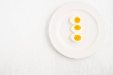 Kaynamış yumurtaların üst görüntüsü ve beyaz bir tabakta bir kaşık beyaz ahşap masa, kahvaltı ve sağlık kavramları üzerine yerleştirilmiş.