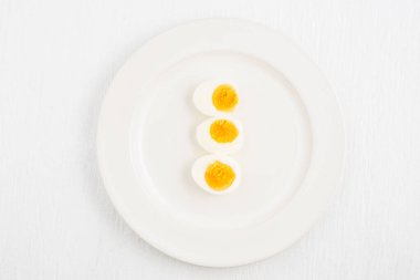 Kaynamış yumurtaların üst görüntüsü ve beyaz bir tabakta bir kaşık beyaz ahşap masa, kahvaltı ve sağlık kavramları üzerine yerleştirilmiş.