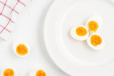 Kaynamış yumurtaların üst görüntüsü ve beyaz bir tabakta bir kaşık beyaz ahşap masa, kahvaltı ve sağlık kavramları üzerine yerleştirilmiş.