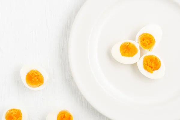 Top view of soft-boiled eggs and a spoon on a white plate placed on a white wooden table, breakfast and health concepts