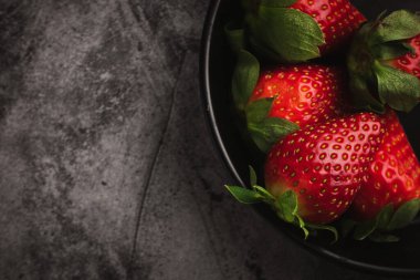 Taze kırmızı çilekler kasede. Koyu taş masa üzerindeki çilek meyveleri metin için fotokopi alanı. en üstteki görünüm.